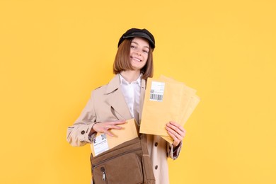 Photo of Happy postwoman with bag and envelopes on yellow background