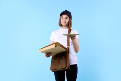 Photo of Happy postwoman with bag giving envelope on light blue background