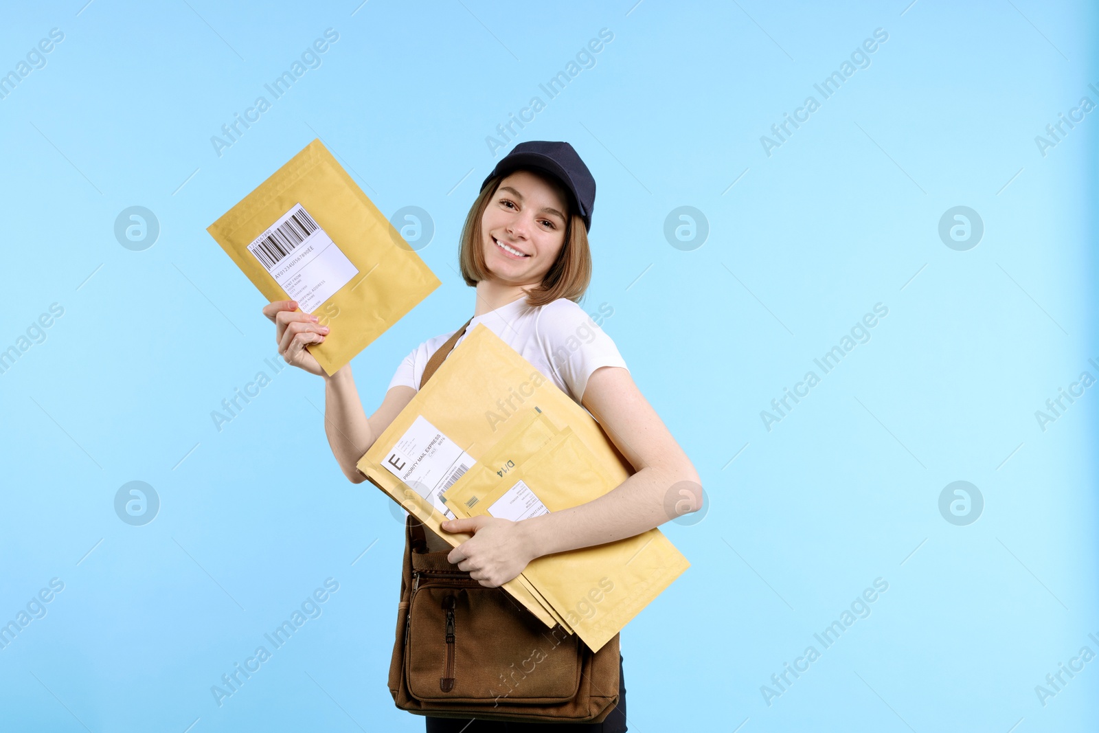 Photo of Happy postwoman with bag and envelopes on light blue background