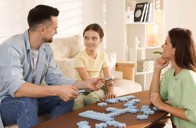 Photo of Happy parents and their daughter solving puzzle together at wooden table indoors