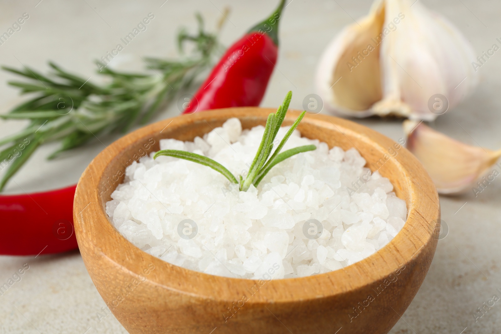 Photo of Sea salt in bowl, rosemary, chili pepper and garlic on grey table, closeup