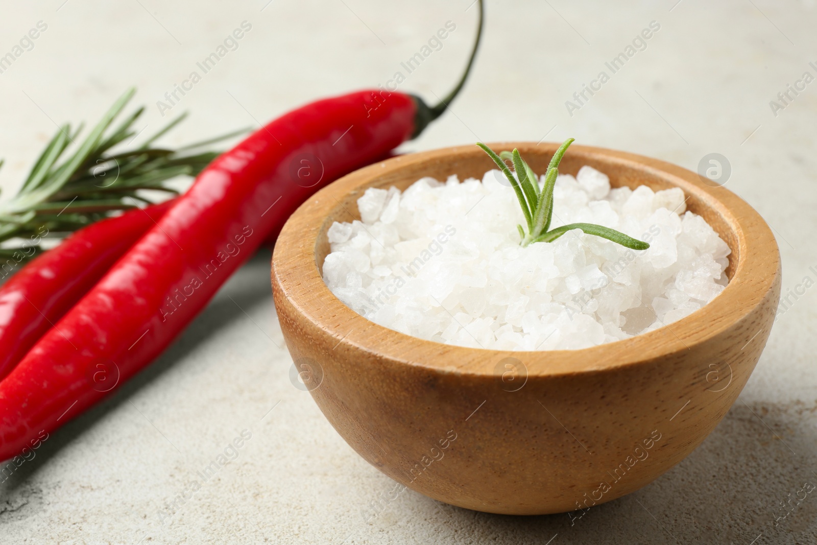 Photo of Sea salt in bowl, rosemary and chili peppers on grey table, closeup