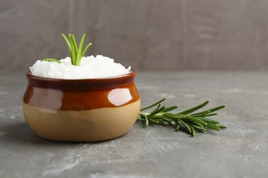 Photo of Sea salt in bowl and rosemary on grey table, closeup. Space for text