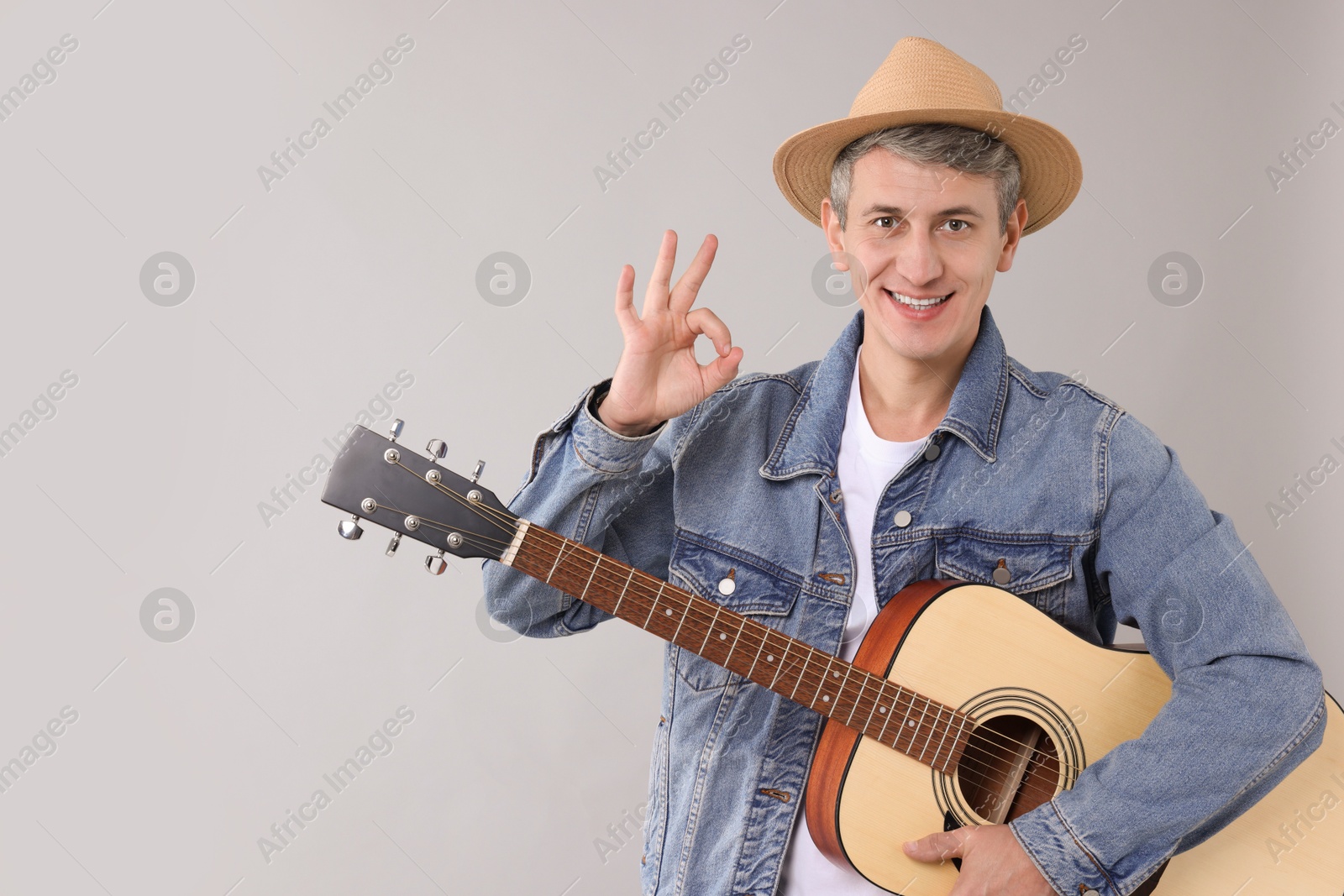 Photo of Happy man with guitar showing okay gesture on light grey background. Space for text