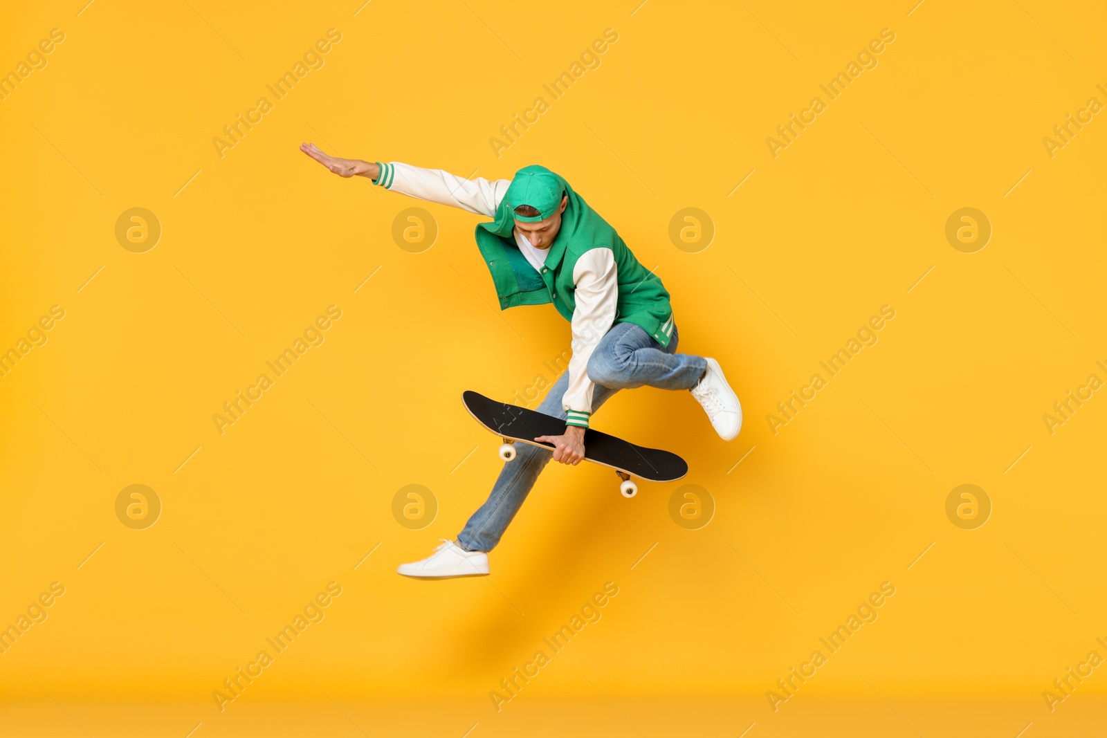 Photo of Handsome man jumping with skateboard on orange background