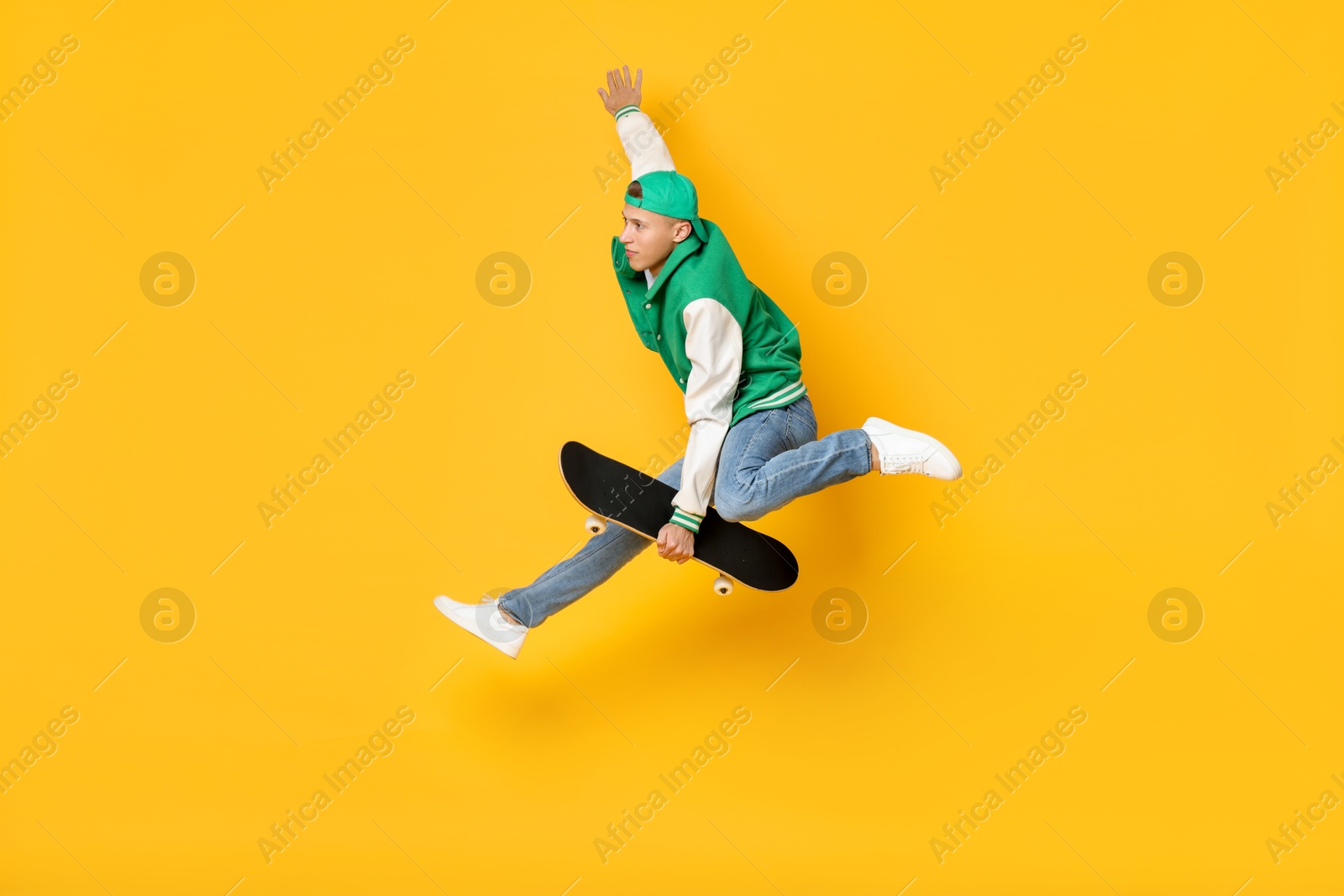 Photo of Handsome man jumping with skateboard on orange background