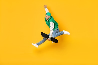 Photo of Handsome man jumping with skateboard on orange background