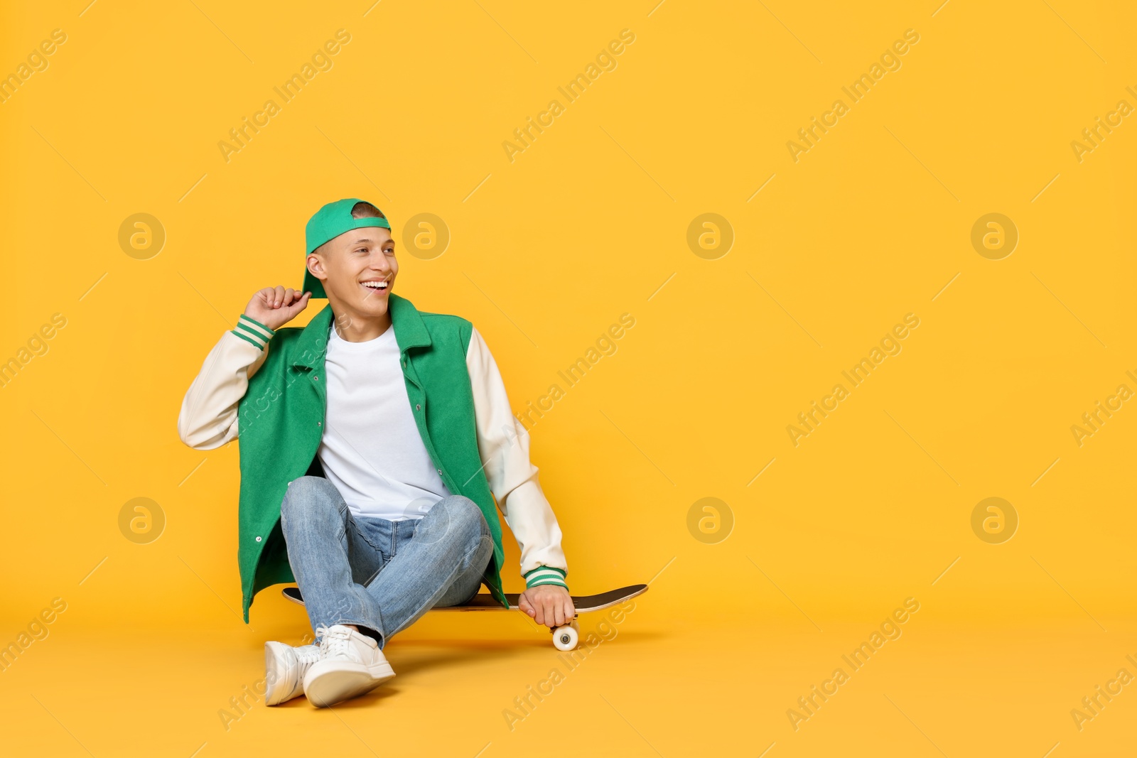 Photo of Happy man sitting on skateboard against orange background. Space for text