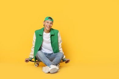 Photo of Happy man sitting on skateboard against orange background. Space for text