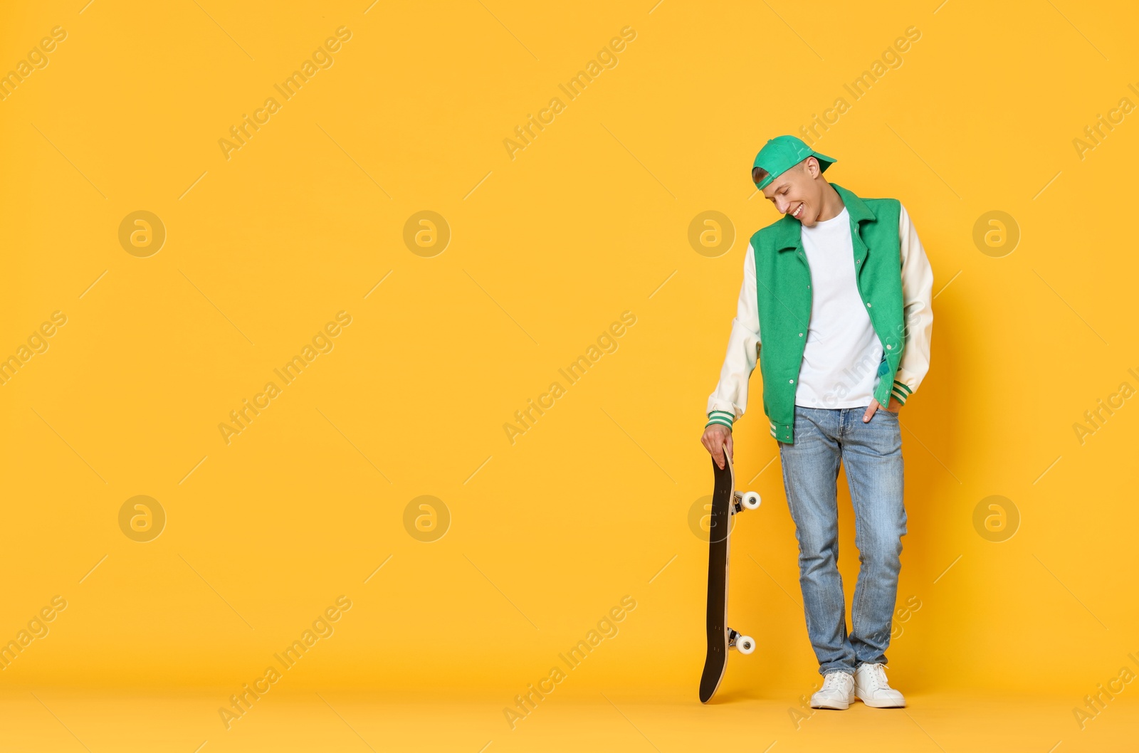 Photo of Happy man with skateboard on orange background. Space for text