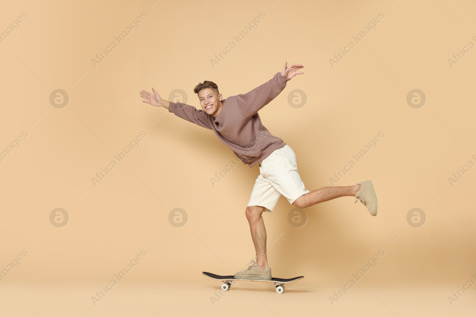 Photo of Happy man riding skateboard on beige background