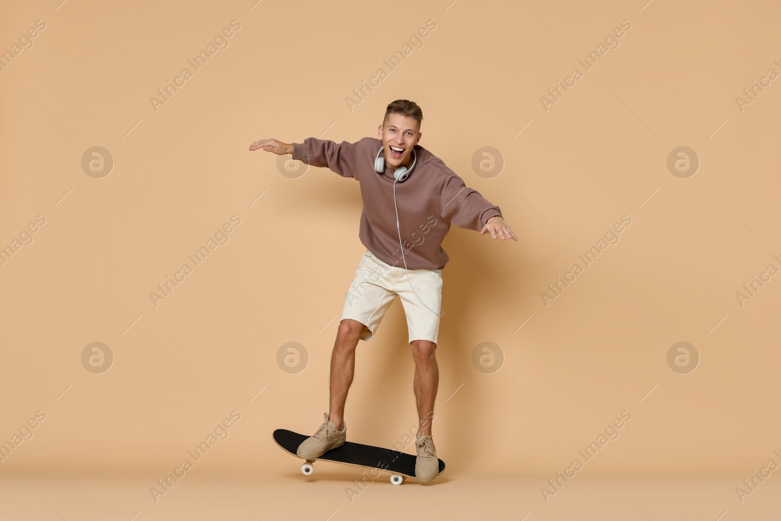 Photo of Happy man riding skateboard on beige background