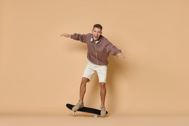 Photo of Happy man riding skateboard on beige background