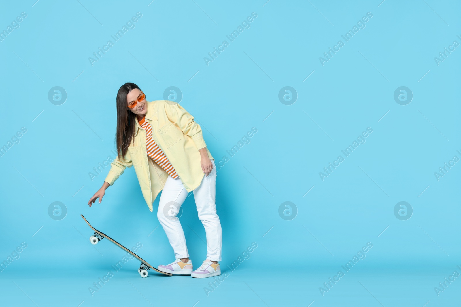 Photo of Smiling woman with skateboard on light blue background. Space for text