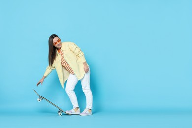 Photo of Smiling woman with skateboard on light blue background. Space for text