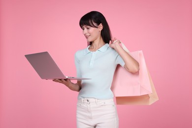 Photo of Internet shopping. Happy woman with laptop and colorful bags on pink background