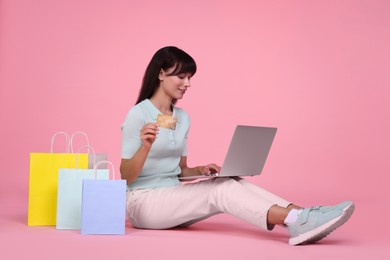 Photo of Internet shopping. Happy woman with credit card, laptop and colorful bags on pink background