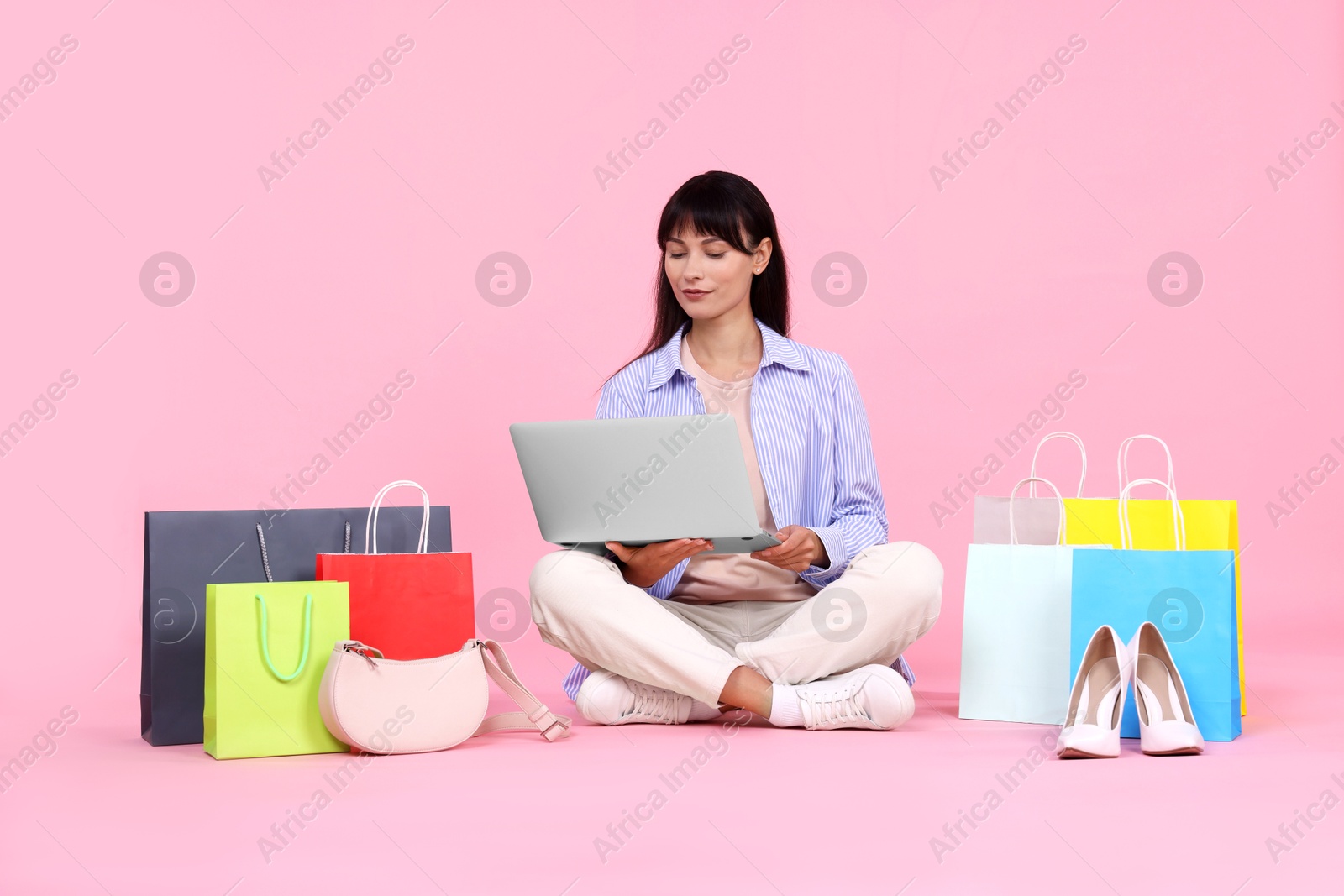 Photo of Internet shopping. Beautiful woman with laptop and colorful bags on pink background