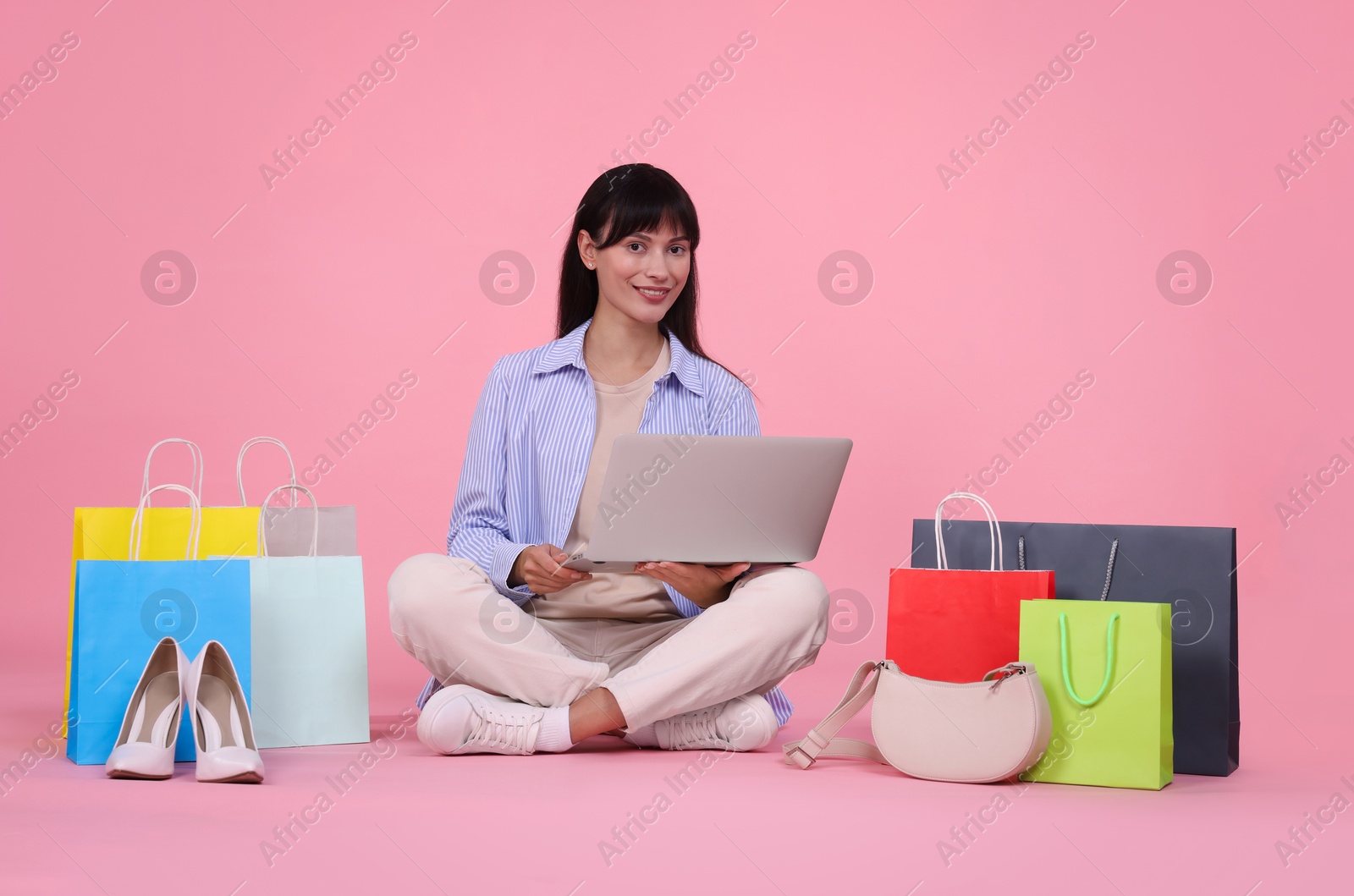 Photo of Internet shopping. Happy woman with laptop and colorful bags on pink background