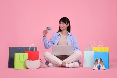 Photo of Internet shopping. Happy woman with credit card, laptop and colorful bags on pink background