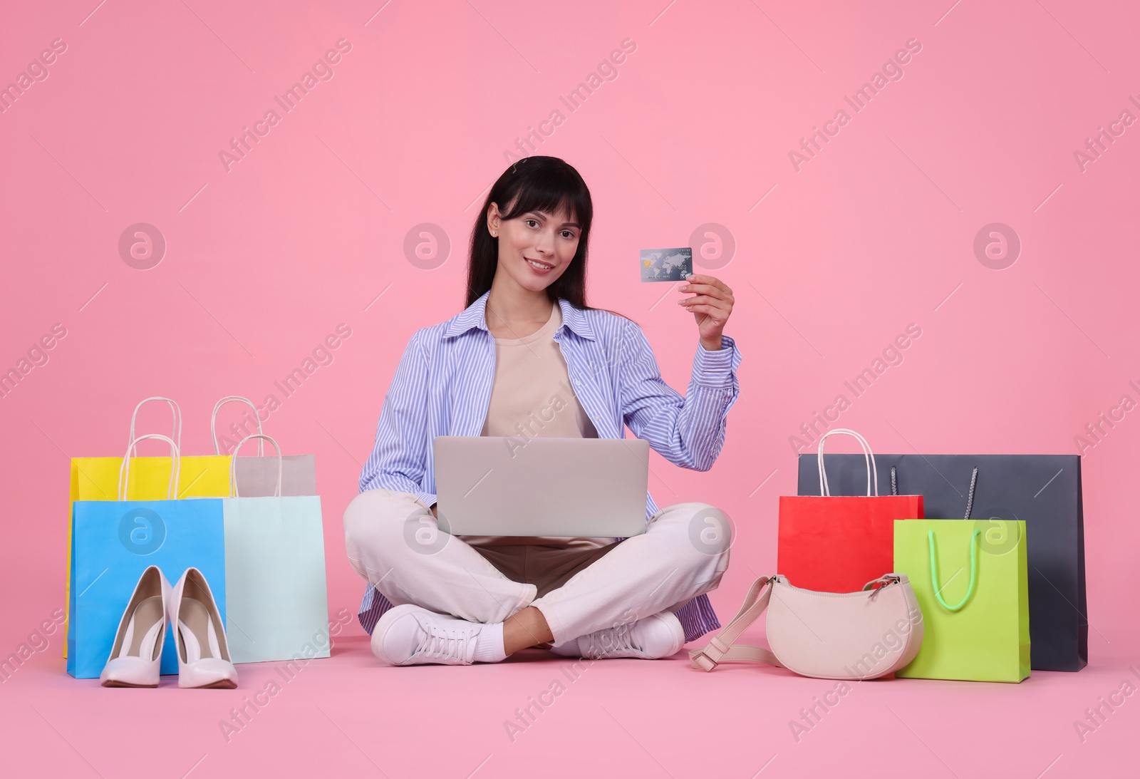 Photo of Internet shopping. Happy woman with credit card, laptop and colorful bags on pink background