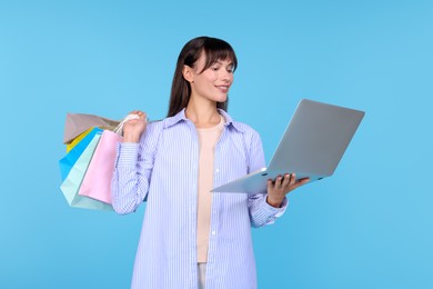 Photo of Internet shopping. Happy woman with laptop and colorful bags on light blue background