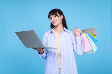 Photo of Internet shopping. Happy woman with laptop and colorful bags on light blue background