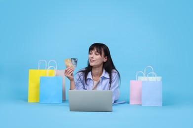 Photo of Internet shopping. Happy woman with credit cards, laptop and colorful bags on light blue background