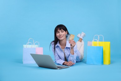 Photo of Internet shopping. Happy woman with credit cards, laptop and colorful bags on light blue background