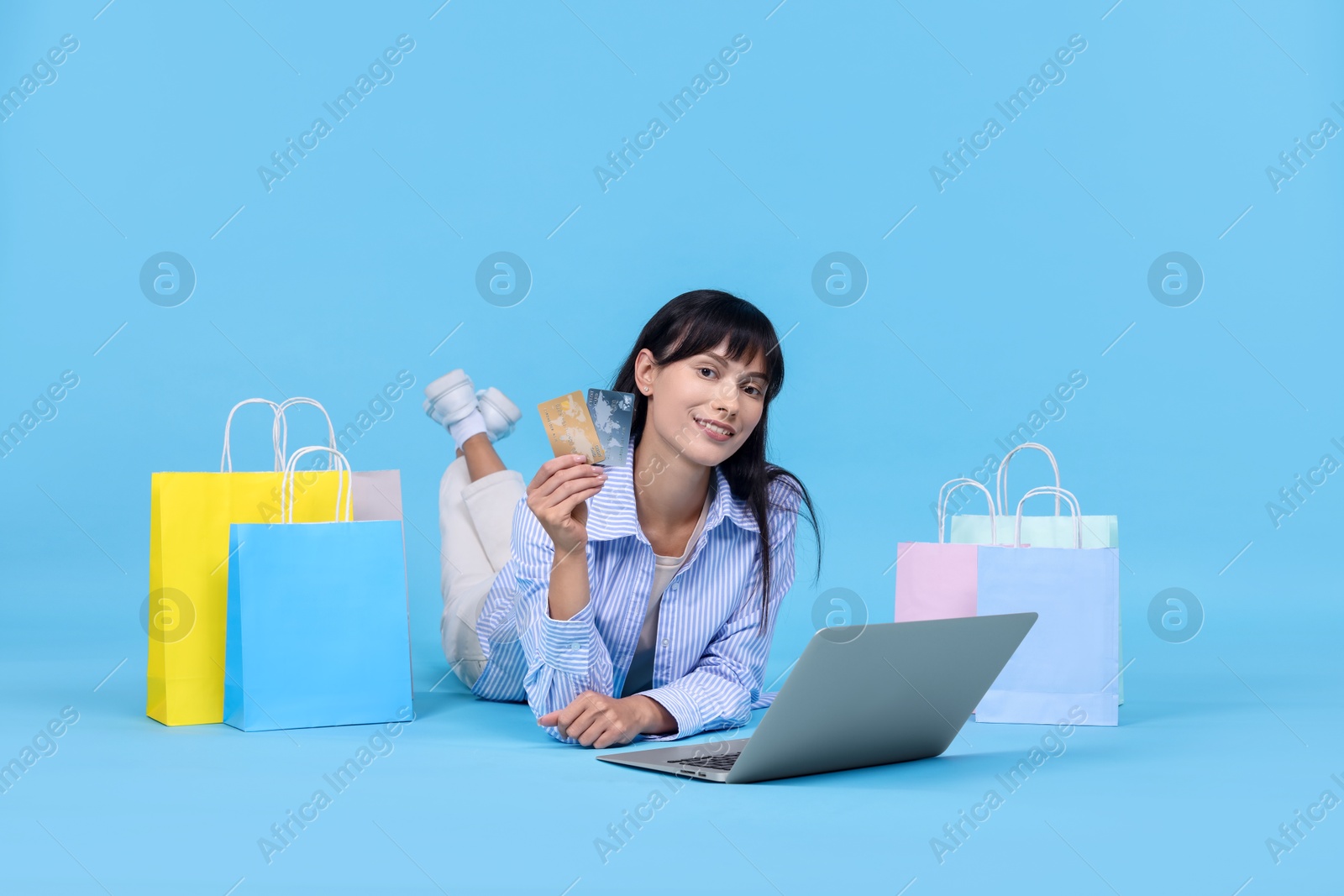 Photo of Internet shopping. Happy woman with credit cards, laptop and colorful bags on light blue background