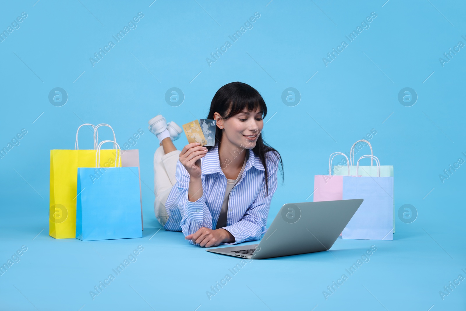 Photo of Internet shopping. Happy woman with credit cards, laptop and colorful bags on light blue background