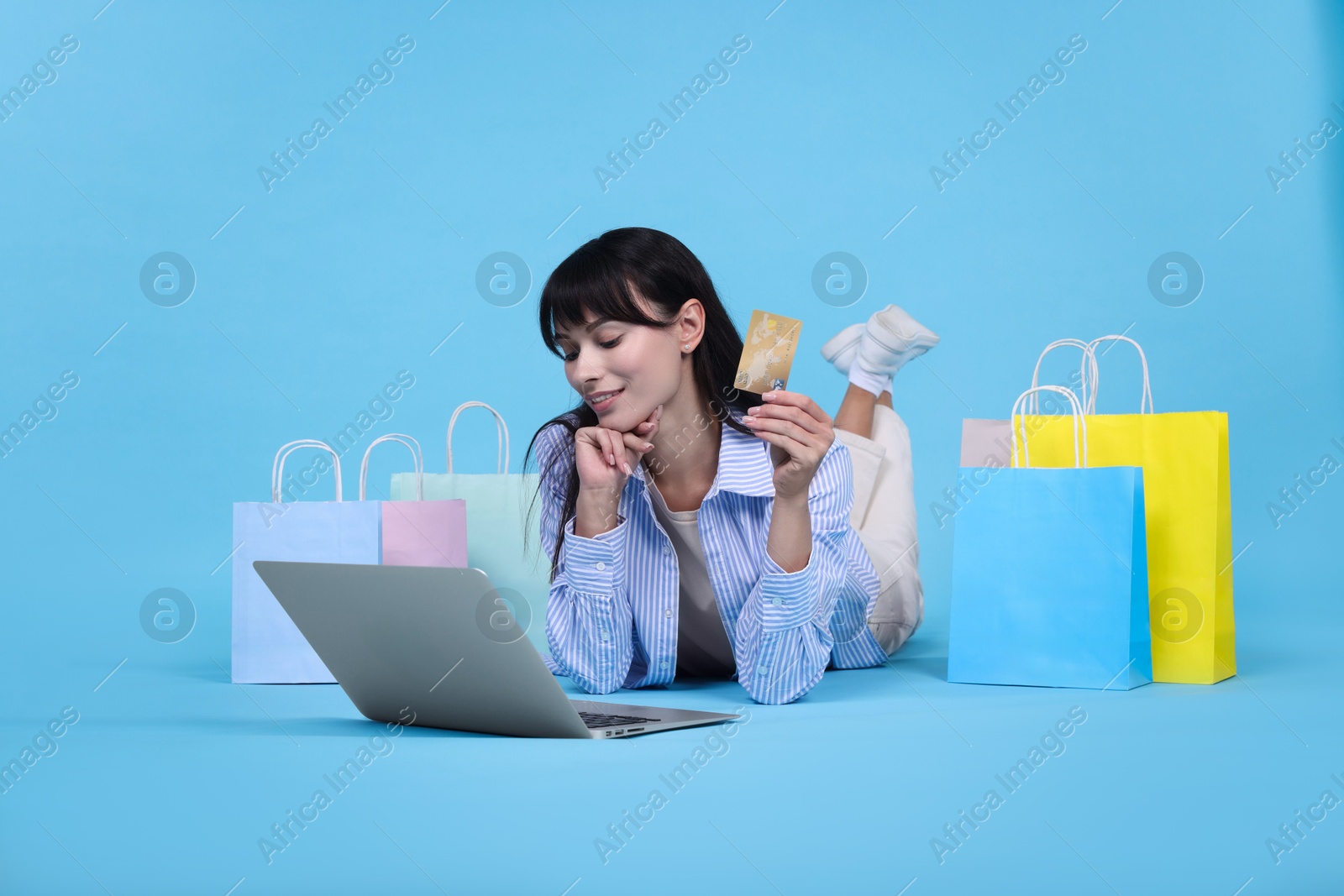 Photo of Internet shopping. Happy woman with credit card, laptop and colorful bags on light blue background