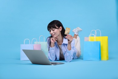 Photo of Internet shopping. Happy woman with credit card, laptop and colorful bags on light blue background