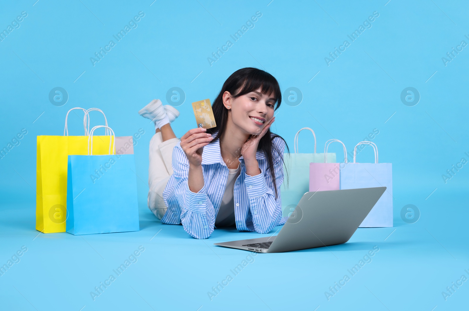 Photo of Internet shopping. Happy woman with credit card, laptop and colorful bags on light blue background