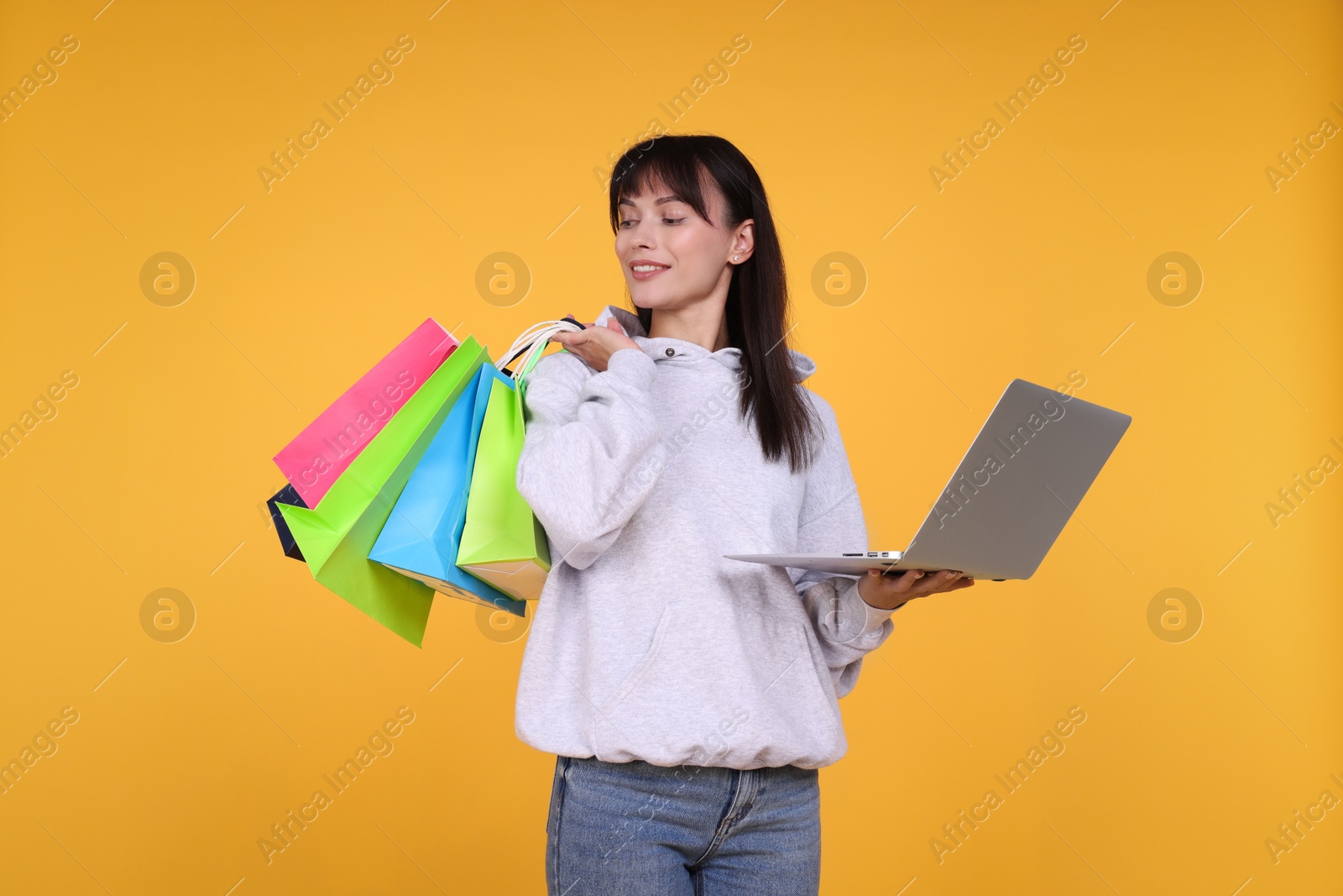 Photo of Internet shopping. Happy woman with laptop and colorful bags on orange background