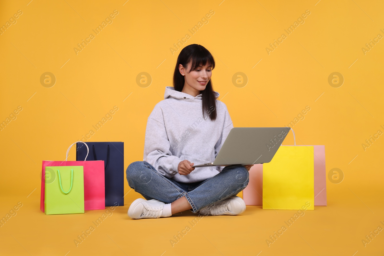 Photo of Internet shopping. Happy woman with laptop and colorful bags on orange background