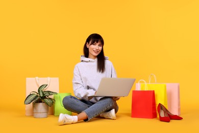 Photo of Internet shopping. Happy woman with laptop and colorful bags on orange background