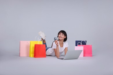 Photo of Internet shopping. Happy woman with credit card, laptop and colorful bags on grey background