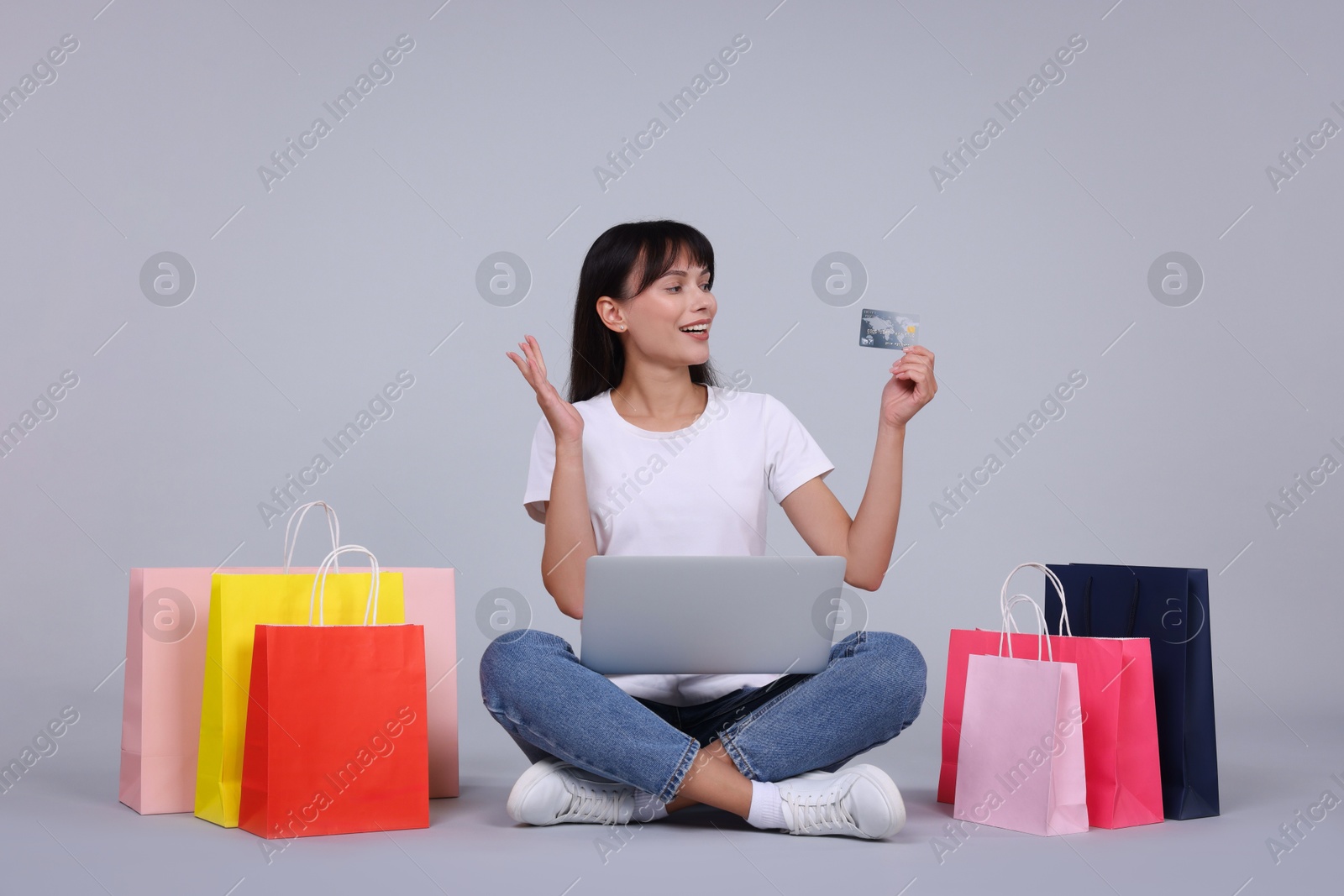 Photo of Internet shopping. Happy woman with credit card, laptop and colorful bags on grey background