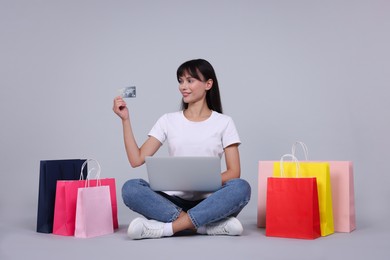 Photo of Internet shopping. Happy woman with credit card, laptop and colorful bags on grey background