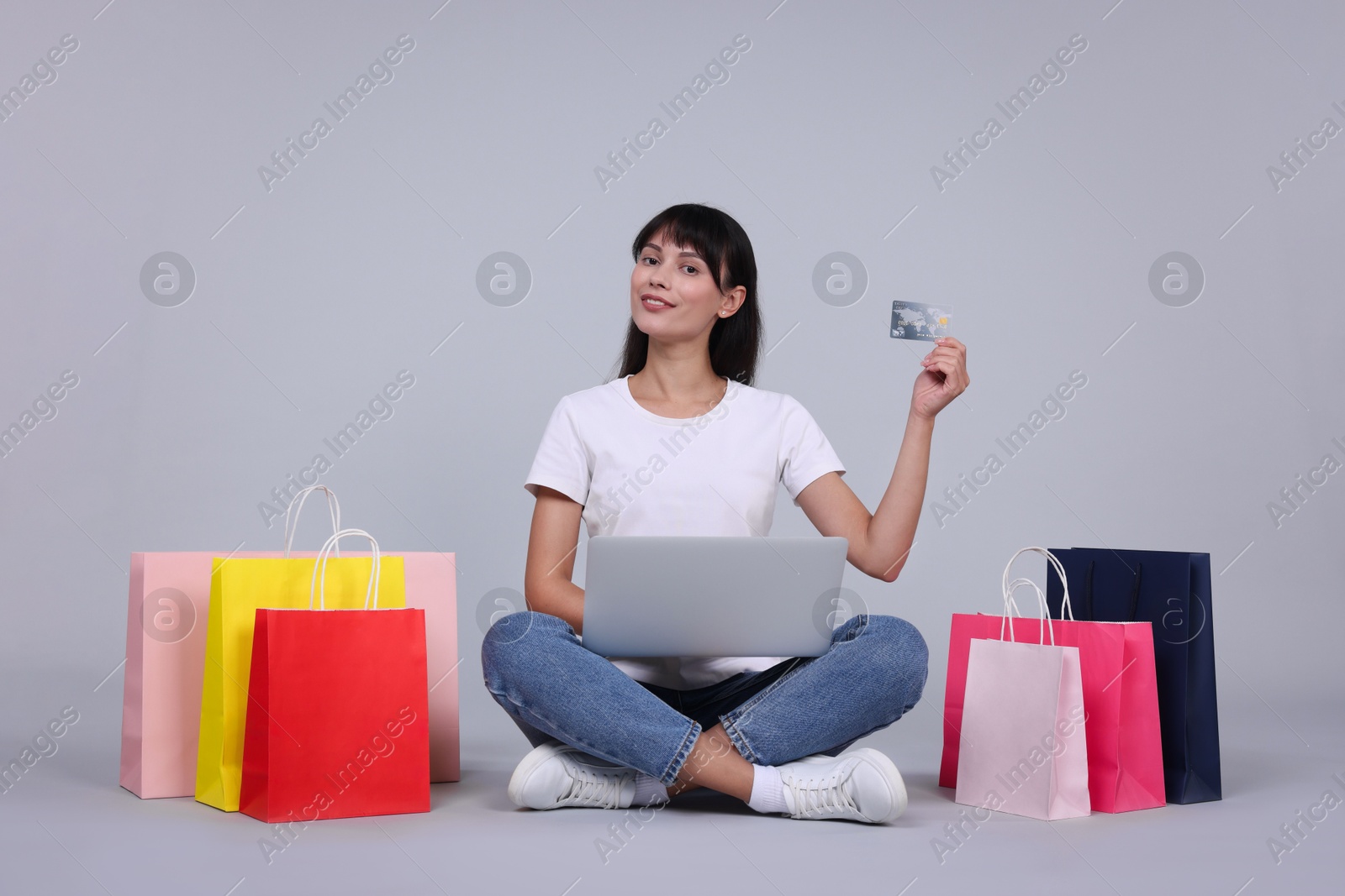 Photo of Internet shopping. Happy woman with credit card, laptop and colorful bags on grey background