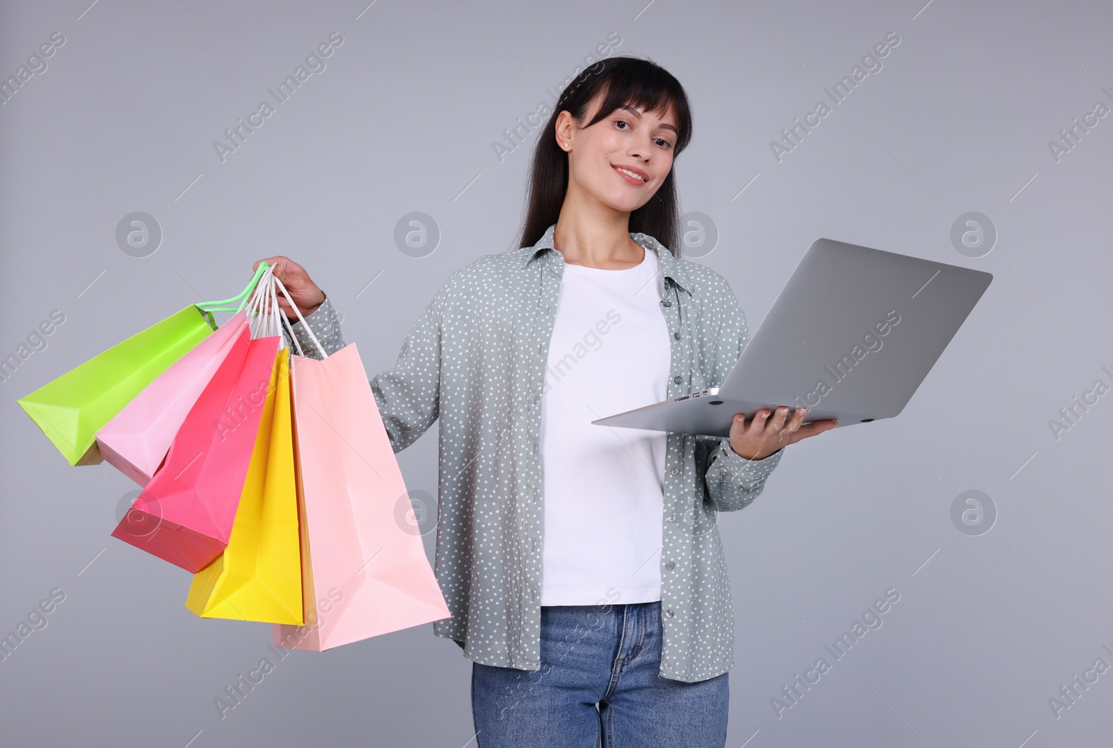 Photo of Internet shopping. Happy woman with laptop and colorful bags on grey background