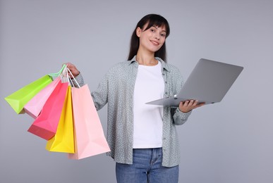 Photo of Internet shopping. Happy woman with laptop and colorful bags on grey background