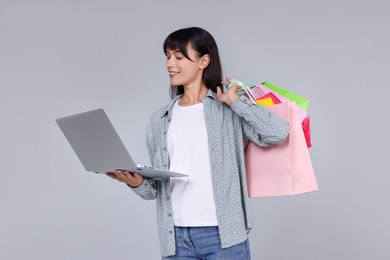 Internet shopping. Happy woman with laptop and colorful bags on grey background