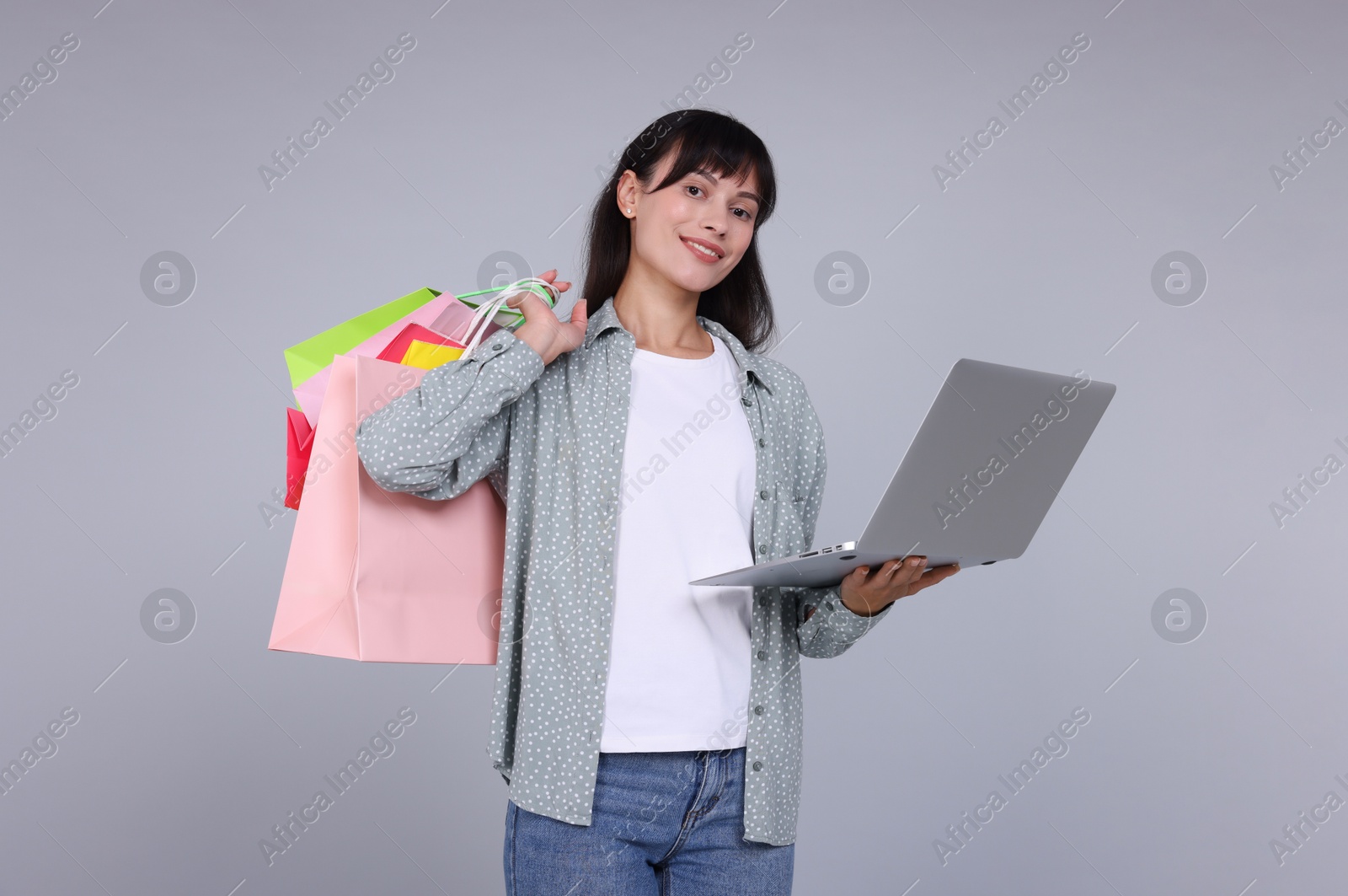 Photo of Internet shopping. Happy woman with laptop and colorful bags on grey background