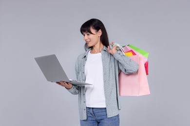 Photo of Internet shopping. Happy woman with laptop and colorful bags on grey background