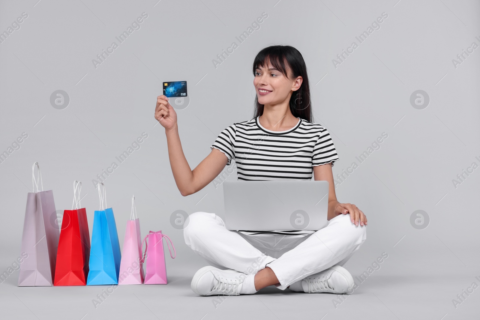 Photo of Internet shopping. Happy woman with credit card, laptop and colorful bags on grey background