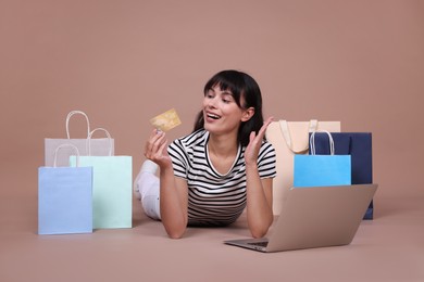 Photo of Internet shopping. Happy woman with credit card, laptop and colorful bags on beige background