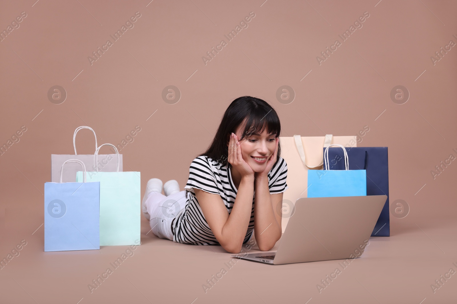 Photo of Internet shopping. Happy woman with laptop and colorful bags on beige background