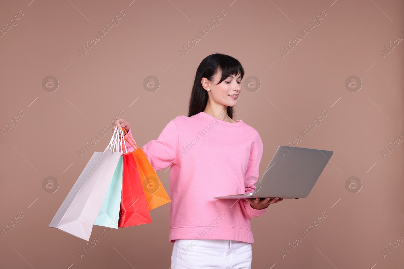 Photo of Internet shopping. Happy woman with laptop and colorful bags on beige background